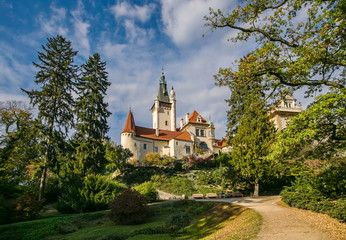 Scenic landscape of famous romantic Pruhonice castle, Czech Republic, Europe, standing on hill in a park, sunny fall day, blue sky, colorful trees, foot path with shadows of trees