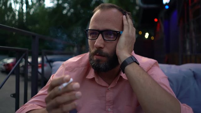 Sad, unhappy man smoking cigarette in cafe in city