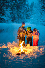 Three kids drinking hot chocolate in the winter snow at dusk