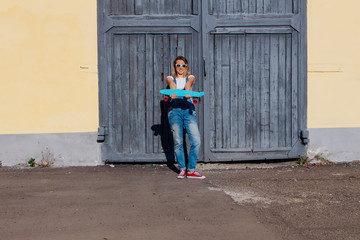 Portrait of a smiling woman standing with her skateboard next to the old wooden wall.