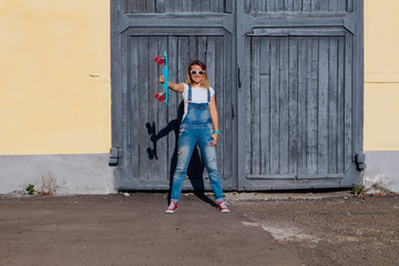 Portrait of a smiling woman standing with her skateboard next to the old wooden wall.