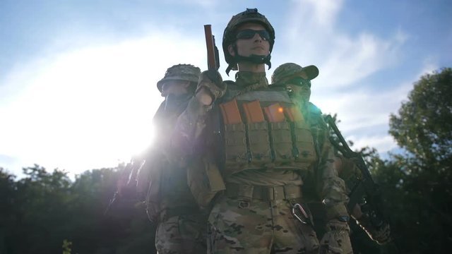 Defend your homeland. Low andgle portrait of special forces marines fully equipped and armed standing in circle at sunset over blue sky background. Brave army soldiers in combat uniform posing.
