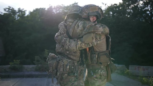 Positive army soldier in combat uniform meeting his brother in arms after combat. Special forces marine warmly greeting his fellow, embracing him, happy to see that he's alive and kicking after battle