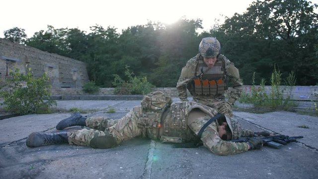 Grief-stricken army soldier with weapons in camouflage sitting on his knees near fallen comrade in arms during combat. Military marine in sorrow for lost fellow screaming and blaming sky for casualty.