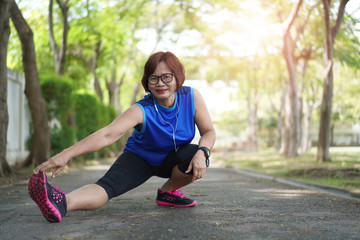 Senior asian woman stretch muscles at park and listening to music. Athletic senior exercising together outdoor. Fit senior runners stretching before running outdoors.