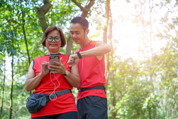 Senior asian woman with man or personal trainer checking time from mobile phone  and smart watch. Checking heart rate while elderly care exercise sport activity concept