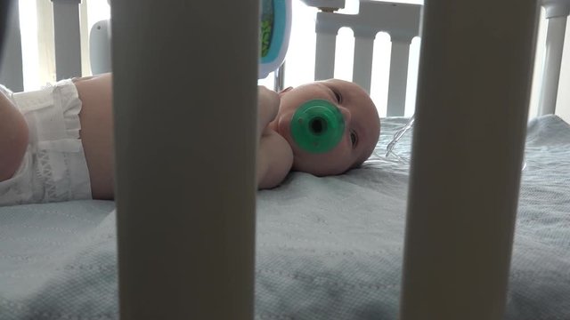 A swaddled baby sucking on a pacifier in a hospital crib.  He starts to cry when he drops his pacifier. Shot in high speed photography.