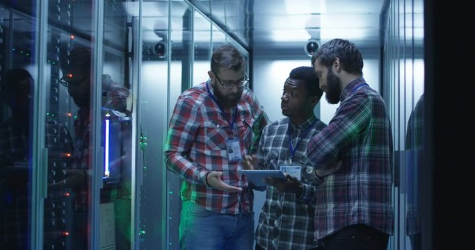 Group of diverse men in checkered shirts using tablet and diagnosing modern system in server room - Powered by Adobe
