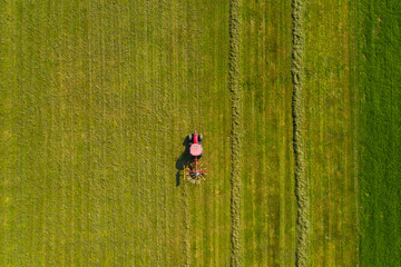 Top down aerial view of a red tractor cultivating farmland with a spinning rack