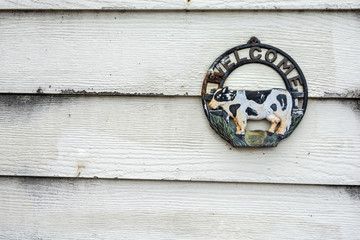 Old rusty metal cow welcome sign hanging on white wood background.