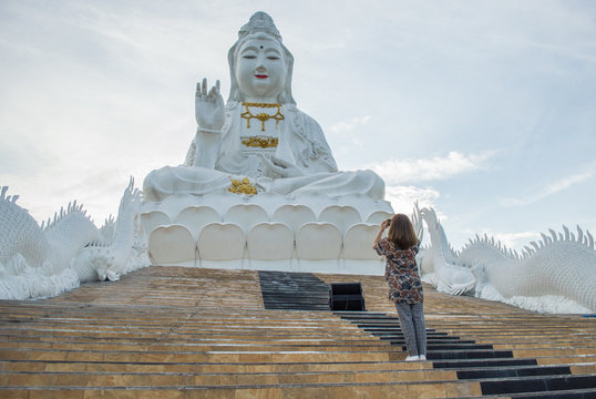 Asian woman taking a pictures of big goddess statue named "Guanyin" at Wat Huay Pla Kung temple in Chiang Rai province of Thailand.