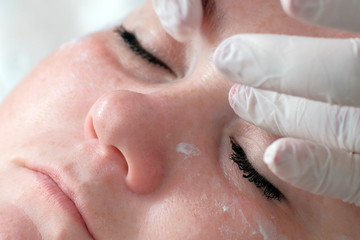 Fototapeta premium Close-up. The hands of a beautician or a doctor in white gloves put eye cream on the face of a full woman. Skin cleaning in the cosmetology center. Cosmetological therapeutic beauty procedure.