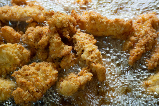 fried chicken with hot bubbling cooking oil in pan; closed up and selective focus.