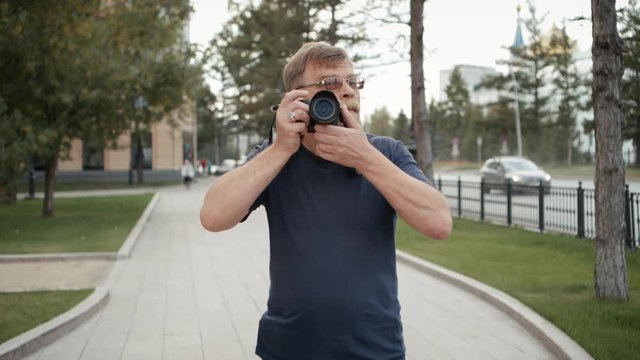 An adult man takes pictures in a city street.