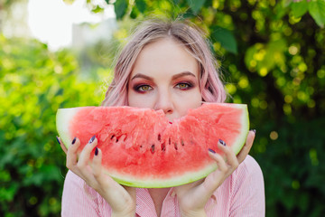 Beautiful young woman with pink hair enjoying watermelon