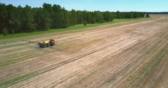 red tractor trailer for spraying chemicals drives on harvested field