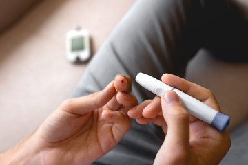 Handsome stylish young teen caucasian white brunette guy man european taking a blood sample with a glucometer to measure sugar level,lancet on finger diabetes, glycemia meter top first view shot