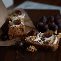 small sandwiches with cream cheese, decorated with grapes, walnuts and flax on a wooden background
