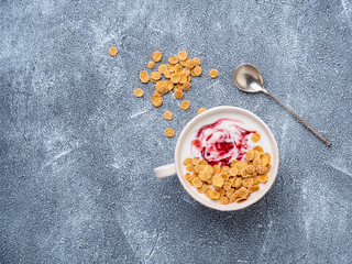 greek yogurt with jam and muesli in white bowl on grey blue concrete stone table, top view, copy space