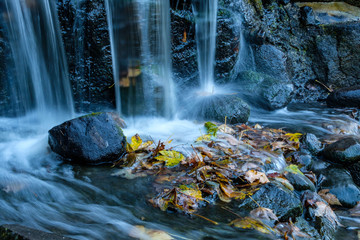 small waterfall rushing down to the rock with piles of fall leaves at the bottom