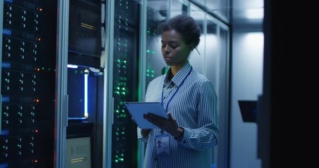 Portrait of African American woman working as IT engineer and standing among server racks in data center room - Powered by Adobe
