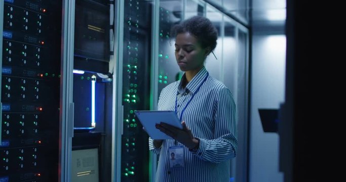 Portrait of African American woman working as IT engineer and standing among server racks in data center room