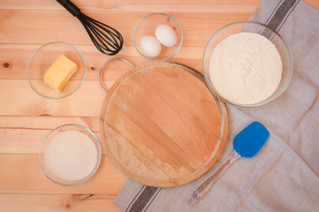 Cutting board surrounded by baking ingredients, whisk and spatula. Top view, copy space.