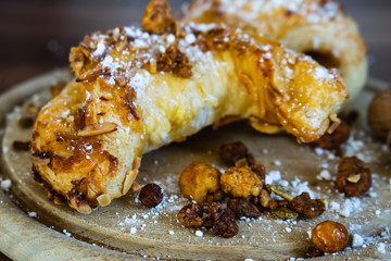 Mandelhörnchen mit Puderzucker und Nüssen auf einem Holzbrett