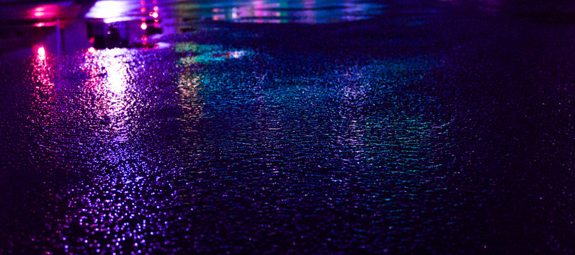 Background of wet asphalt with neon light. Blurred background, night lights of a big city, reflection, puddles. Dark neon bokeh. © MiaStendal