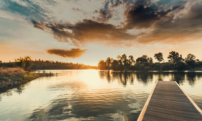 Obraz premium Wooden jetty at sunset with the orange sky and the sun hiding behind the eucalyptus trees