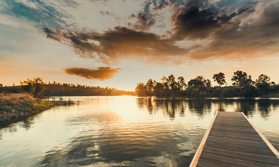 Wooden jetty at sunset with the orange sky and the sun hiding behind the eucalyptus trees