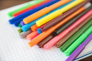 Multicolored felt pens with notebook on wooden background. Recreation concept drawing