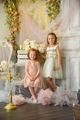 Fototapeta na wymiar Girls on the queen throne with flowers in rich fairytale interior studio shot