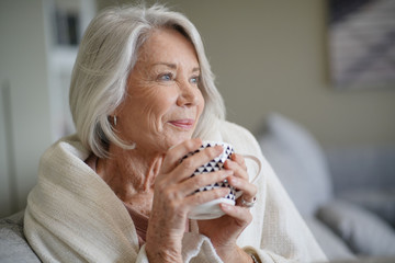  Cosy looking senior woman at home with hot drink