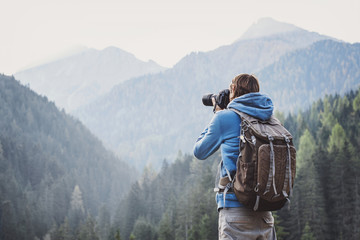 Young cheerful man photographer taking photographs with digital camera in a mountains. Travel and active lifestyle concept - Powered by Adobe