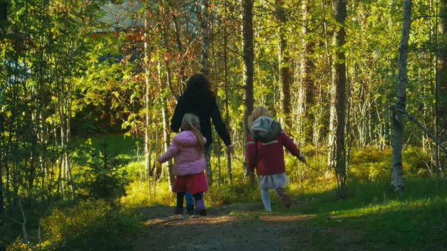 A mother and her two daughters walking on a path through a forest with Autumn colors and golden light. Family togetherness and quality time enjoying the outdoors. Slow motion.