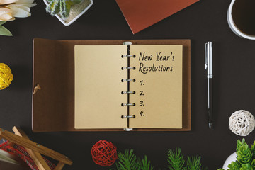 New Year's Resolutions text on rustic notepad with pen and coffee on black background.