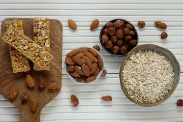 Muesli bars and their ingredients.Healthy diet food.Muesli bars , oatmeal, almonds, hazelnuts and sunflower seeds in round  clay cups on a white wooden background.Healthy foods