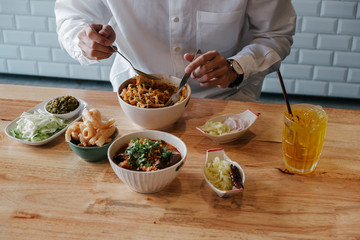 Asian Man eat  Thai Food -Khao Soi with pork snack (Thai Noodle Curry Soup with chicken), Nam Prik Num (Green chili dip) and  Hunglei curry (North curry With tender pork) over the wooden table