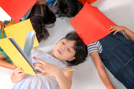 Kids reading book laying on the white floor ,head to head, in a circle group, preschool library,Kindergarten school education concept