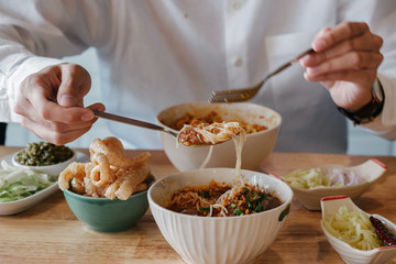 Asian Man eat Thai Food -Khao Soi with pork snack (Thai Noodle Curry Soup with chicken), Nam Prik Num (Green chili dip) and  Hunglei curry (North curry With tender pork) over the wooden table