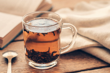 A cup with black brewed tea on a wooden table with book and a warm sweater. Concept cozy autumn or winter vacation.