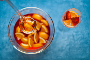 Woman pouring fruity punch into glass on blue table, top view. Orange cocktail. Soft focus.