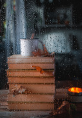 Stacked books and hot tea through rainy window