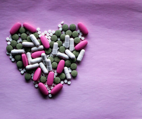 White, pink and green pills laid out in the shape of a heart on a pink background. multi-colored drugs. concept - heart disease, heart disorders and drugs, cardiology.