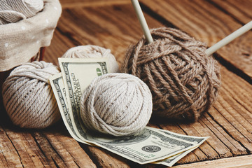 Fototapeta na wymiar Profitable hobby. Earnings on needlework. Balls of natural color yarn, knitting needles and money on a wooden table.