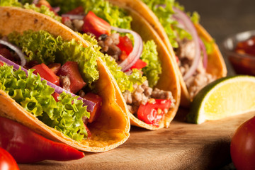 Photo of Mexican tacos with ground beef, onion, tomatoes, chili, red sauce, lettuce and lime on wooden background. Spicy and fast food concept.