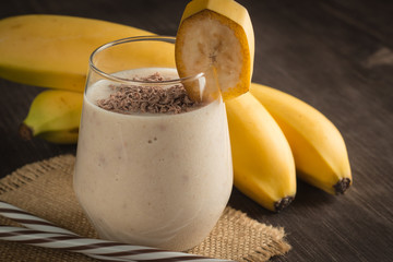 Photo of fresh Made Chocolate Banana Smoothie on a wooden table with cookies, banana and coconut. Milkshake. Protein diet. Healthy food concept. Drink, coffee beans, chocolate.