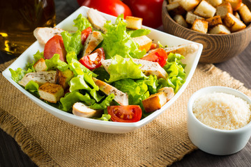 Fresh salad with delicious chicken breast, ruccola, spinach, cabbage, arugula and tomato on wooden background. Oil, salt and pepper.