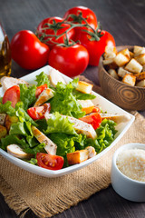 Fresh salad with delicious chicken breast, ruccola, spinach, cabbage, arugula and tomato on wooden background. Oil, salt and pepper.